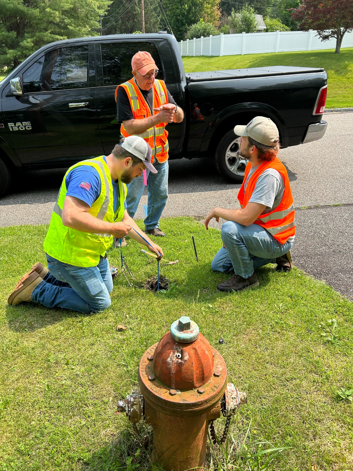 Three water operators in safety vests working at a curb stop beside a fire hydrant